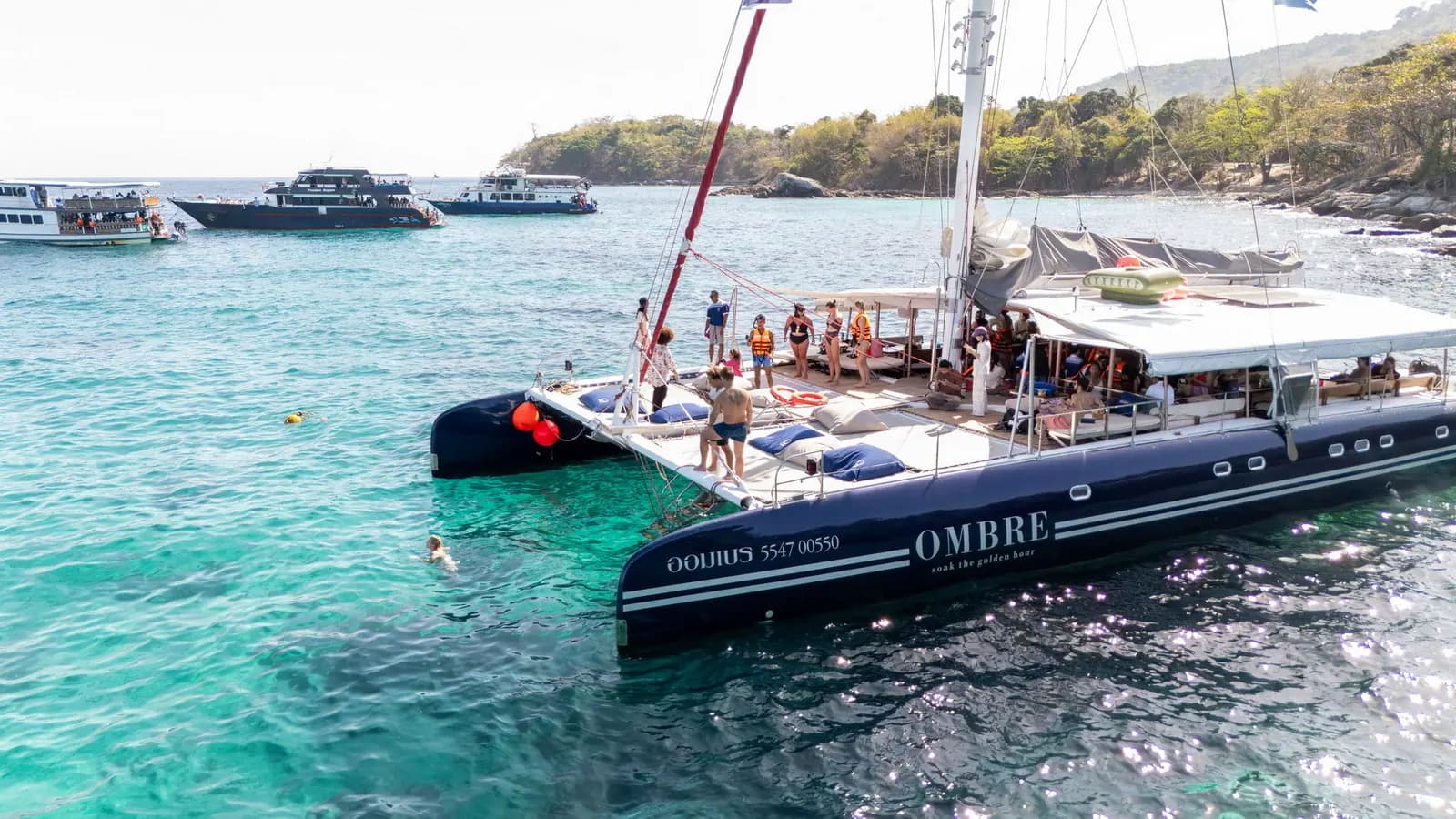 OMBRE catamaran at anchor beside turquoise water and a wooded shore