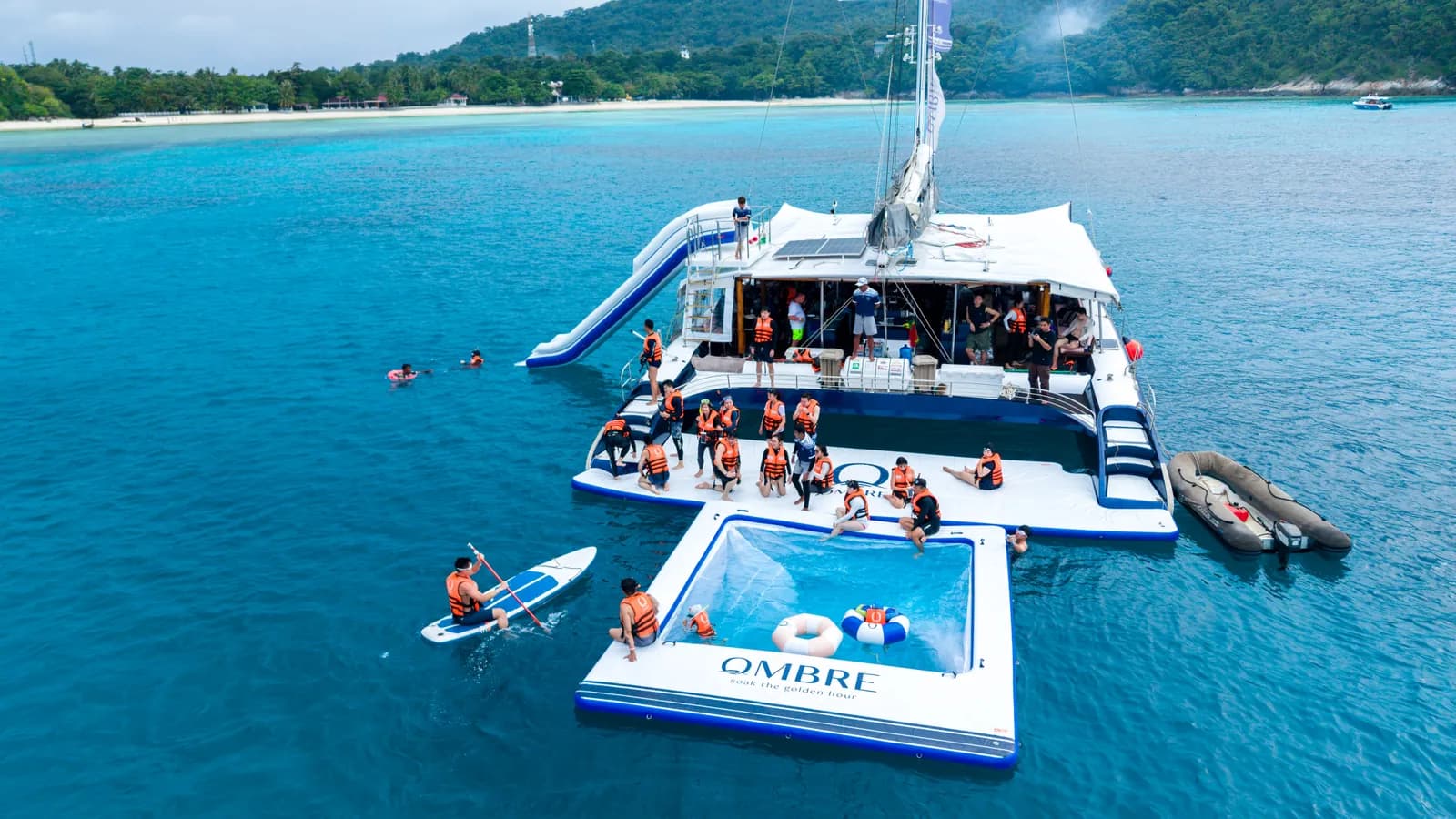 Aerial view of the OMBRE catamaran with its floating swim platform and guests in the water