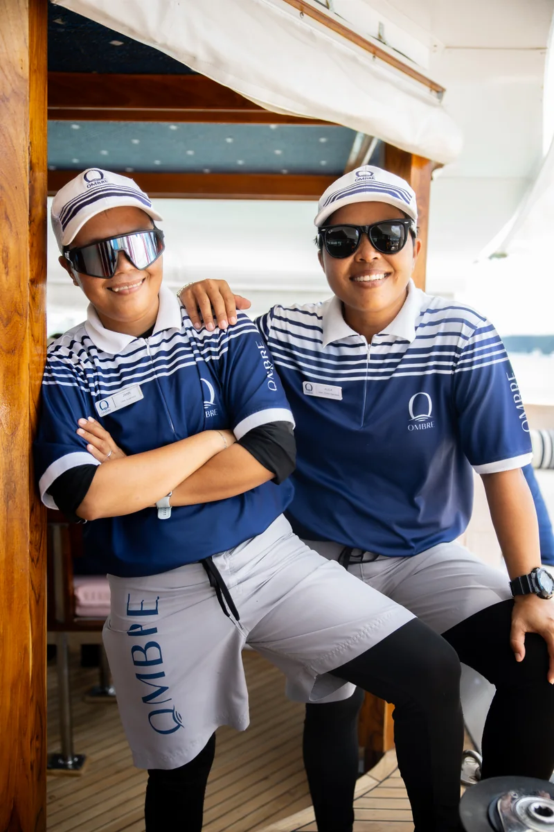 Two OMBRE crew members in navy uniforms aboard the catamaran