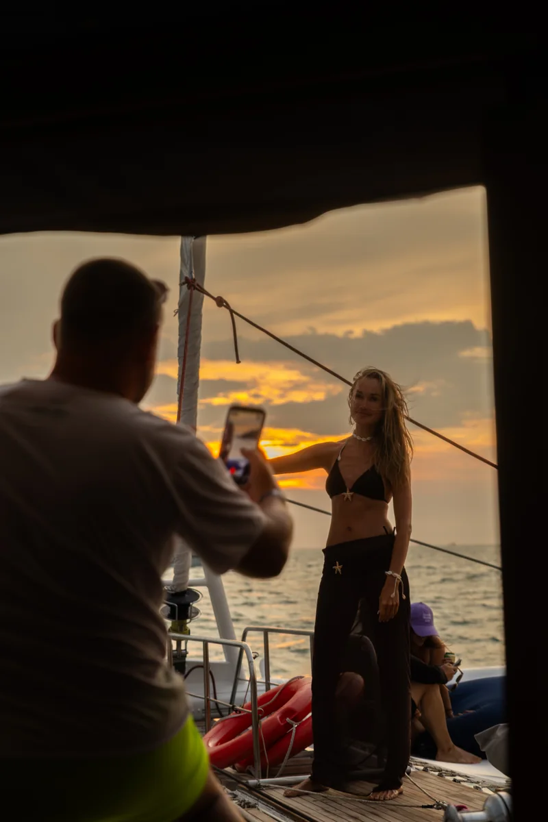 A guest photographs another guest beside the yacht rail at sunset