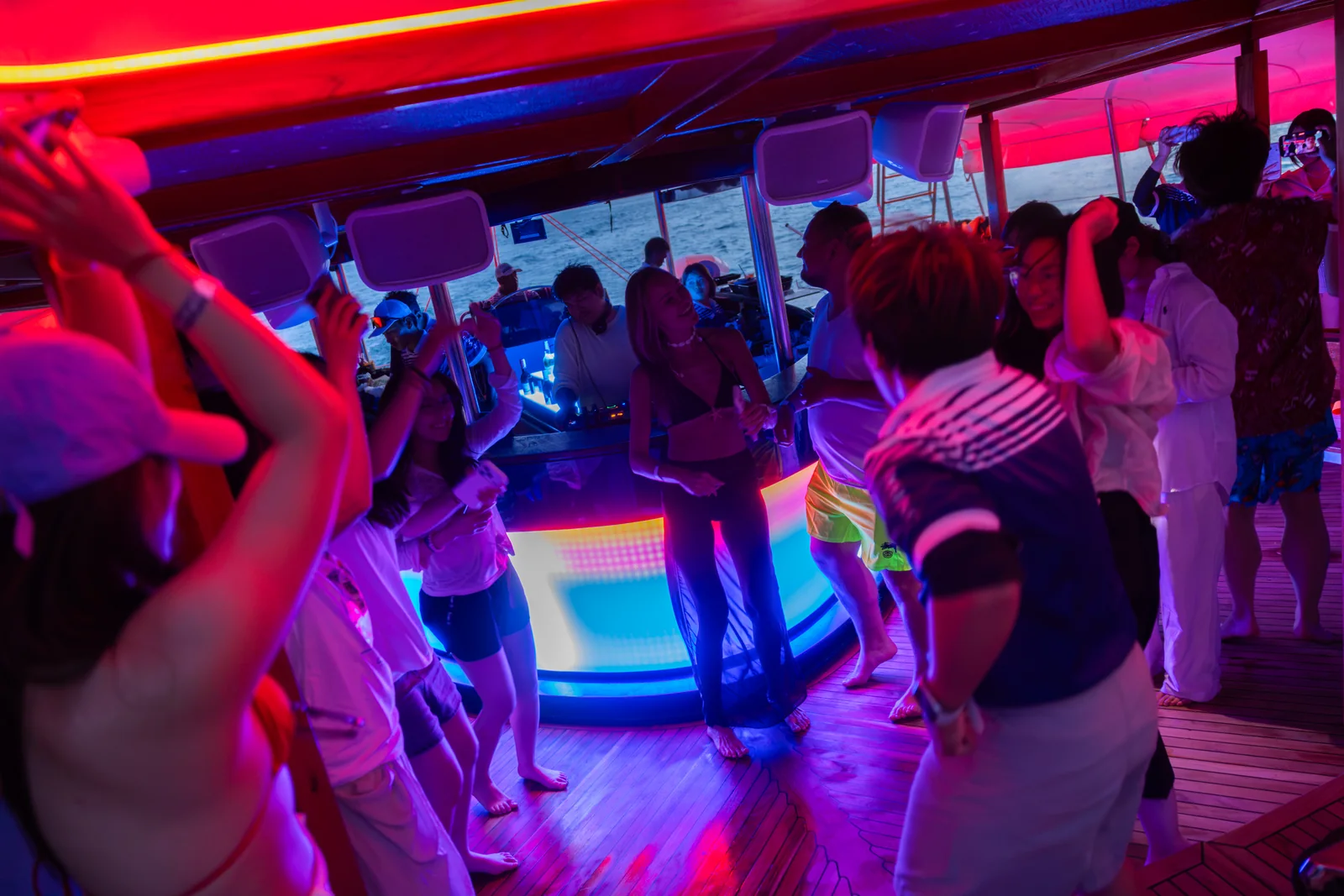 Guests dancing inside the catamaran under pink and blue evening lights