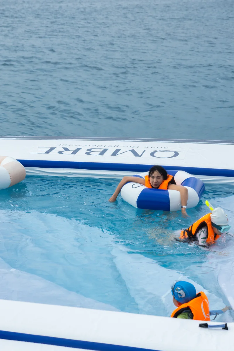Guests swimming beside a blue and white floating OMBRE platform