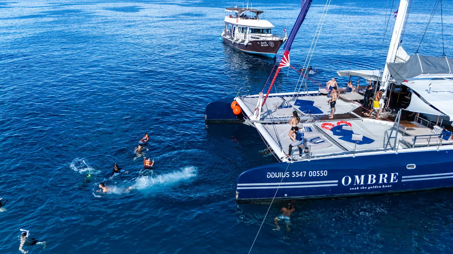 Swimmers in open blue water beside the OMBRE catamaran